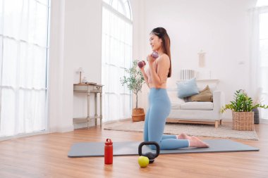 Evde egzersiz yapan Asyalı kadın, huzurlu bir oturma odası ortamında güç, denge ve genel sağlığa odaklanıyor, aktif bir yaşam tarzı, sağlıklı alışkanlıklar ve dikkatli bir fitness eğitimi sergiliyor..