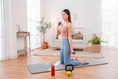 Evde egzersiz yapan Asyalı kadın, huzurlu bir oturma odası ortamında güç, denge ve genel sağlığa odaklanıyor, aktif bir yaşam tarzı, sağlıklı alışkanlıklar ve dikkatli bir fitness eğitimi sergiliyor..