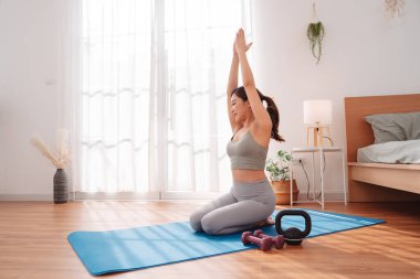 Antrenmandan sonra yatak odasında yoga minderinde uzanan bir kadın çocuk pozu veriyor. Sağlıklı yaşam tarzı, vücut iyileştirme, farkındalık ve evde esneklik eğitimi.