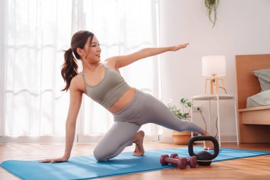 Antrenmandan sonra yatak odasında yoga minderinde uzanan bir kadın çocuk pozu veriyor. Sağlıklı yaşam tarzı, vücut iyileştirme, farkındalık ve evde esneklik eğitimi.