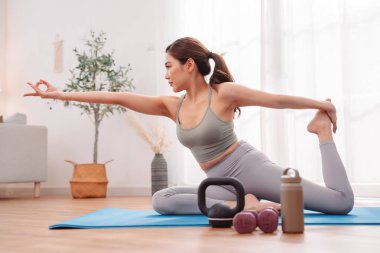 Kadın, yoga minderinin üzerinde dambıl ve kettlebell kullanarak spor yapıyor. Sağlıklı yaşam tarzı, dayanıklılık eğitimi, sağIık, spor ve iç mekanda vücut tonlaması..