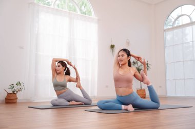 Women stretching together on yoga mats, performing flexibility pose. Healthy lifestyle, partner workout, balance, and mindful fitness routine.