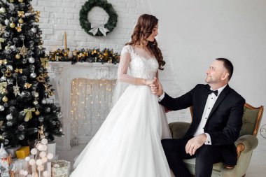 Sevgili gelin ve damat, Noel 'de Noel ağacıyla süslenmiş arka planda stüdyoda poz veriyorlar. Mutluluğun ve aşkın tadını çıkar.