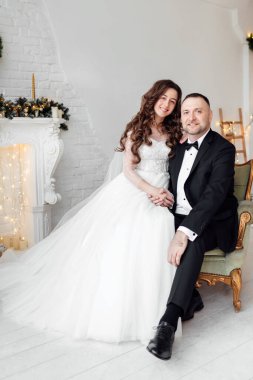 Sevgili gelin ve damat, Noel 'de Noel ağacıyla süslenmiş arka planda stüdyoda poz veriyorlar. Mutluluğun ve aşkın tadını çıkar.