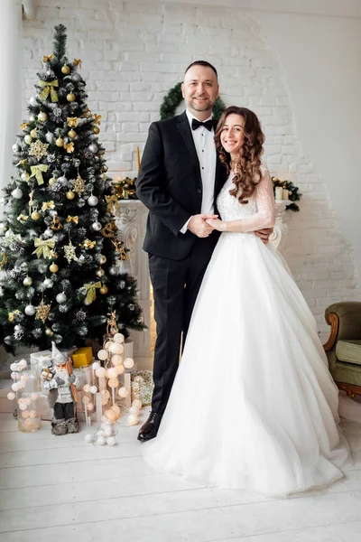 クリスマスの結婚式の日にクリスマスツリーで飾られた背景にスタジオでポーズをとっている愛の花嫁と新郎の若いカップル 幸せと愛の瞬間をお楽しみください — ストック写真