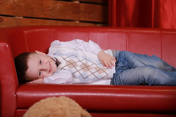 小男孩在红灯笼里的沙发上玩得很开心 背景上的圣诞树和泰迪熊 — 图库照片