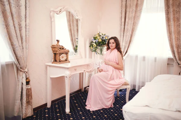 穿着粉红衣服的红头发孕妇坐在窗边一张经典内饰的椅子上 在等孩子 — 图库照片