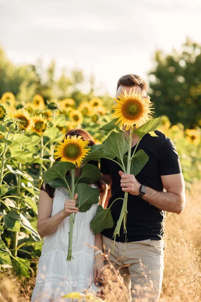 Beautiful couple having fun in sunflowers field. A man and a woman in love walk in a field with sunflowers, a man hugs a woman. selective focus.