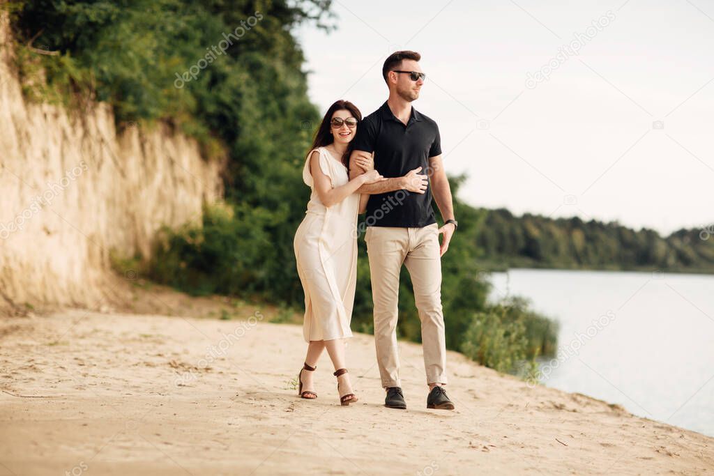 Happy lovers at the beach near lake. Young couple is holding hands and walking on summer day outdoors. A man and woman in love. Concept of love and family. full length. Close Up