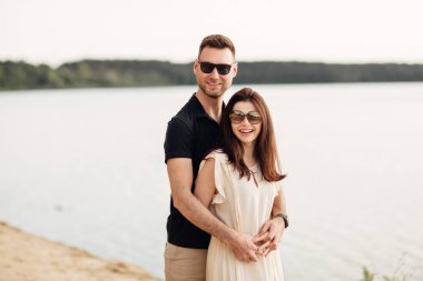 Romantik çift dışarıda kucaklaşıyor. Zarif ve şık bir kadın ve aşık bir adam göl boyunca yürüyorlar. Birlikte mutlu anlar. Aşk hikayesi.