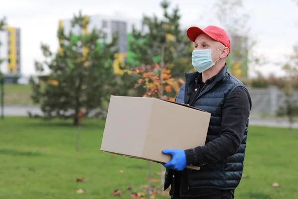 Delivery man in red cap white t-shirt uniform face medical mask gloves hold empty cardboard box on yellow studio background. Service coronavirus. Online shopping. mock up.