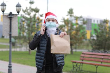 Noel üniformalı teslimatçı, koruma maskesi takan teslimat kağıdı taşıyan akıllı telefonu müşteriye gönderen adam. 2021 'de karantina sırasında yiyecekleri kaldırın.