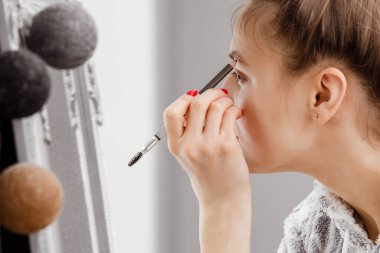 Esmer kadın, akşam randevusu için kirpiklerini aynanın önünde boyuyor. yüz bakımı.