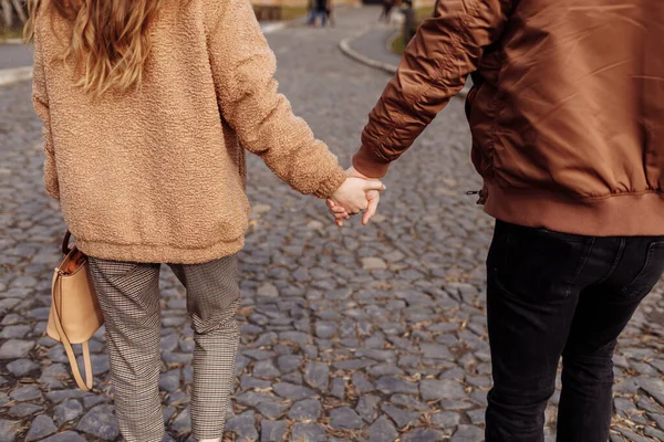 若い恋人のカップルが屋外で手を取り合って通りを歩いている写真 — ストック写真