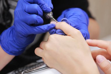 Güzellik salonundaki donanım manikürünü yakından çek. Koruyucu eldivenli manikürcü kadın parmaklarına manikür yapmak için elektrikli tırnak matkabı uyguluyor.