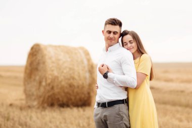 Neşeli bir çiftin fotoğrafı. Bir grup saman yığınıyla altın tarlasında yürüyorlar ve güneşli bir günde birbirlerine sarılıyorlar..