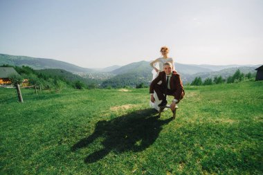 Mutlu şık gelin ve damat yaz güneşli bir günde dağlarda koşup eğleniyor. Muhteşem yeni evli çift gülüyor, gerçek duygular. Duygusal romantik an