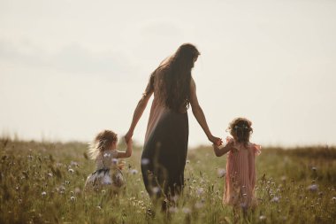 Anne ve çocuklar çayırda bir köy yolunda yürüyen iki kız. Yaz, doğa, aile, tatil. Anneler Günü.
