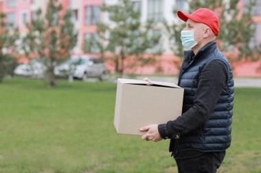 Kırmızı şapkalı teslimatçı, yüzü tıbbi maskeli boş karton kutuyu dışarıda tutuyor. Hizmet koronavirüsü. İnternetten alışveriş. maket yap
