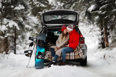 Genç bir çift snowboardcu adam ve kadın kucaklaşarak arabasının bagajında oturuyorlar. Kışın çam ormanında genç bir çiftin yürüyüşü. Kış boş vakitleri