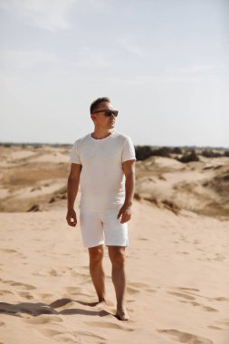 Çölde açık renk elbiseli ve güneş gözlüklü genç bir adam. Özgürlük rahatlama kavramı. Metin veya reklam için yer.
