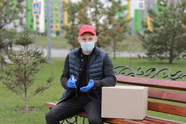 Coronavirus sırasında teslimat servisi kuryesi, COVID-19, salgın, tıbbi koruyucu maskeli teslimatçı, dışarıda karton kutuların yanındaki ellere alkol dezenfektan spreyi sıkan eldivenler..