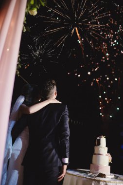 Mutlu kucaklaşmalar gelin ve damat gece gökyüzünde güzel renkli havai fişekler izliyor. Düğün günü, parti.