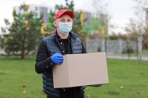 Delivery man in red cap white t-shirt uniform face medical mask gloves hold empty cardboard box on yellow studio background. Service coronavirus. Online shopping. mock up.