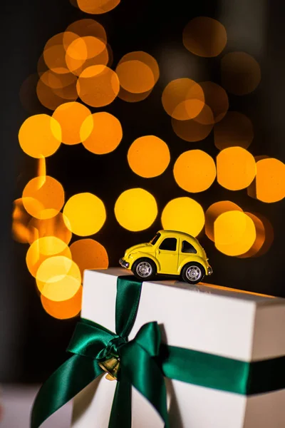 yellow small retro toy car on white gift with green ribbon on a Christmas yellow bokeh background. Delivery. New Year, Christmas, Valentines Day, World Womens Day, Sale concept