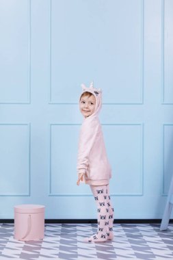 Tek boynuzlu at kostümlü güzel küçük bir kız gülümsüyor ve mavi duvarda eğleniyor. Mutlu çocukluk