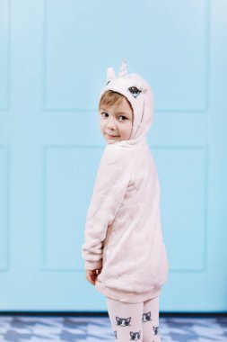 Tek boynuzlu at kostümlü güzel küçük bir kız gülümsüyor ve mavi duvarda eğleniyor. Mutlu çocukluk