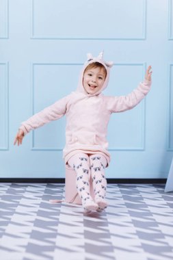 Tek boynuzlu at kostümlü güzel küçük bir kız gülümsüyor ve mavi duvarda eğleniyor. Mutlu çocukluk