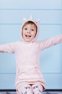 Tek boynuzlu at kostümlü güzel küçük bir kız gülümsüyor ve mavi duvarda eğleniyor. Mutlu çocukluk