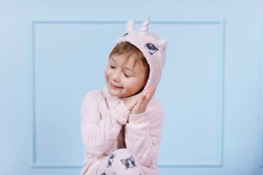 Tek boynuzlu at kostümlü güzel küçük bir kız gülümsüyor ve mavi duvarda eğleniyor. Mutlu çocukluk