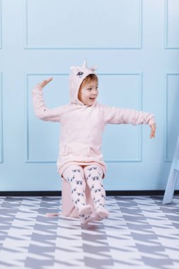 Tek boynuzlu at kostümlü güzel küçük bir kız gülümsüyor ve mavi duvarda eğleniyor. Mutlu çocukluk