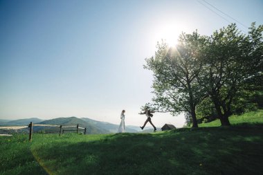 Mutlu şık gelin ve damat yaz güneşli bir günde dağlarda koşup eğleniyor. Muhteşem yeni evli çift gülüyor, gerçek duygular. Duygusal romantik an
