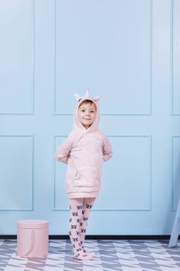 Tek boynuzlu at kostümlü güzel küçük bir kız gülümsüyor ve mavi duvarda eğleniyor. Mutlu çocukluk