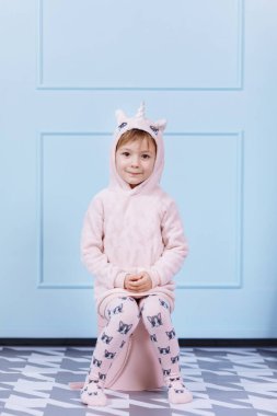 Tek boynuzlu at kostümlü güzel küçük bir kız gülümsüyor ve mavi duvarda eğleniyor. Mutlu çocukluk