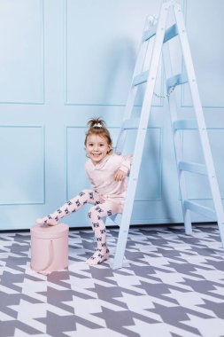 Tek boynuzlu at kostümlü güzel küçük bir kız gülümsüyor ve mavi duvarda eğleniyor. Mutlu çocukluk