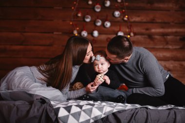 Yatakta genç ve tatlı bir aile ve arkasında Noel geçmişi var. Anne, baba ve bebek birlikte vakit geçirin..