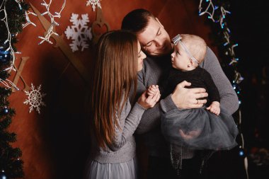 Şirin, genç bir aile babası, anne ve bebek Noel arka planında sarılıp öpüşüyorlar. Mutlu Noeller ve mutlu yıllar.