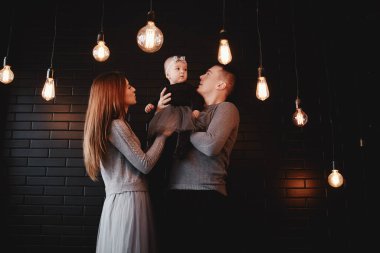 Genç bir ailenin portresi. Baba, anne ve bebek evde birlikte vakit geçiriyorlar. Ön planda retro ampuller var. Noel zamanı