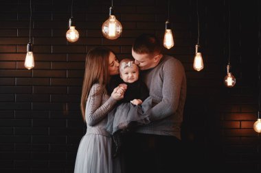 Genç bir ailenin portresi. Baba, anne ve bebek evde birlikte vakit geçiriyorlar. Ön planda retro ampuller var. Noel zamanı