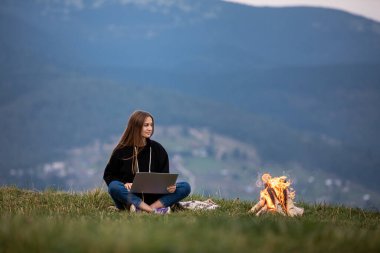 Genç bayan serbest yazar akşamları dağlarda dizüstü bilgisayarda çalışıyor. Kamp ateşinin yanında oturan turist kız eğleniyor. Boşluğu kopyala