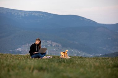 Genç bayan serbest yazar akşamları dağlarda dizüstü bilgisayarda çalışıyor. Kamp ateşinin yanında oturan turist kız eğleniyor. Boşluğu kopyala
