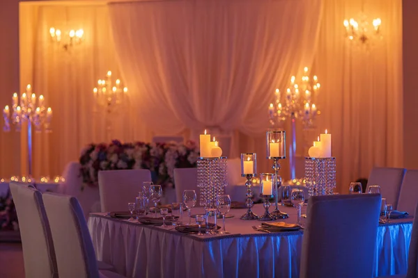 festive wedding table with burning candles, crystal, plates and glasses in yellow light. Crystal candle holder as a center piece at a wedding reception