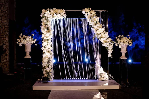 Night wedding ceremony, arch on party decorated with white flowers and lights Open air. Wedding arch decoration. bouquet