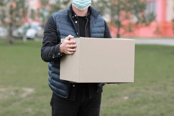 cropped Delivery man in red cap, face medical mask hold empty cardboard box outdoors. Service coronavirus. Online shopping. mock up