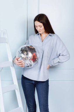 Elinde disko topu olan güzel bir genç kadın. Mavi duvarın arkasında mavi elbiseli, uzun saçlı bir kız..