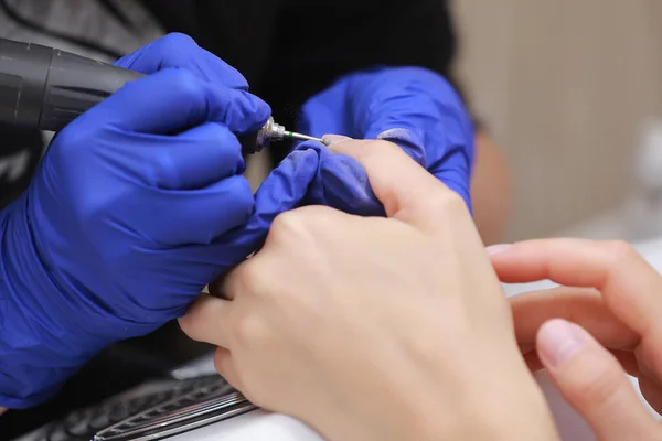 Close Up shot of hardware manicure in a beauty salon. Manicurist in protective gloves is applying electric nail file drill to manicure on female fingers